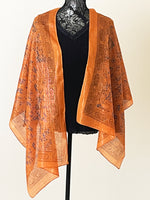 Rust coloured printed scarf woven with sparkly lurex threads draped over a black top.