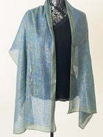 Teal coloured printed scarf woven with sparkly lurex threads draped over a black top.