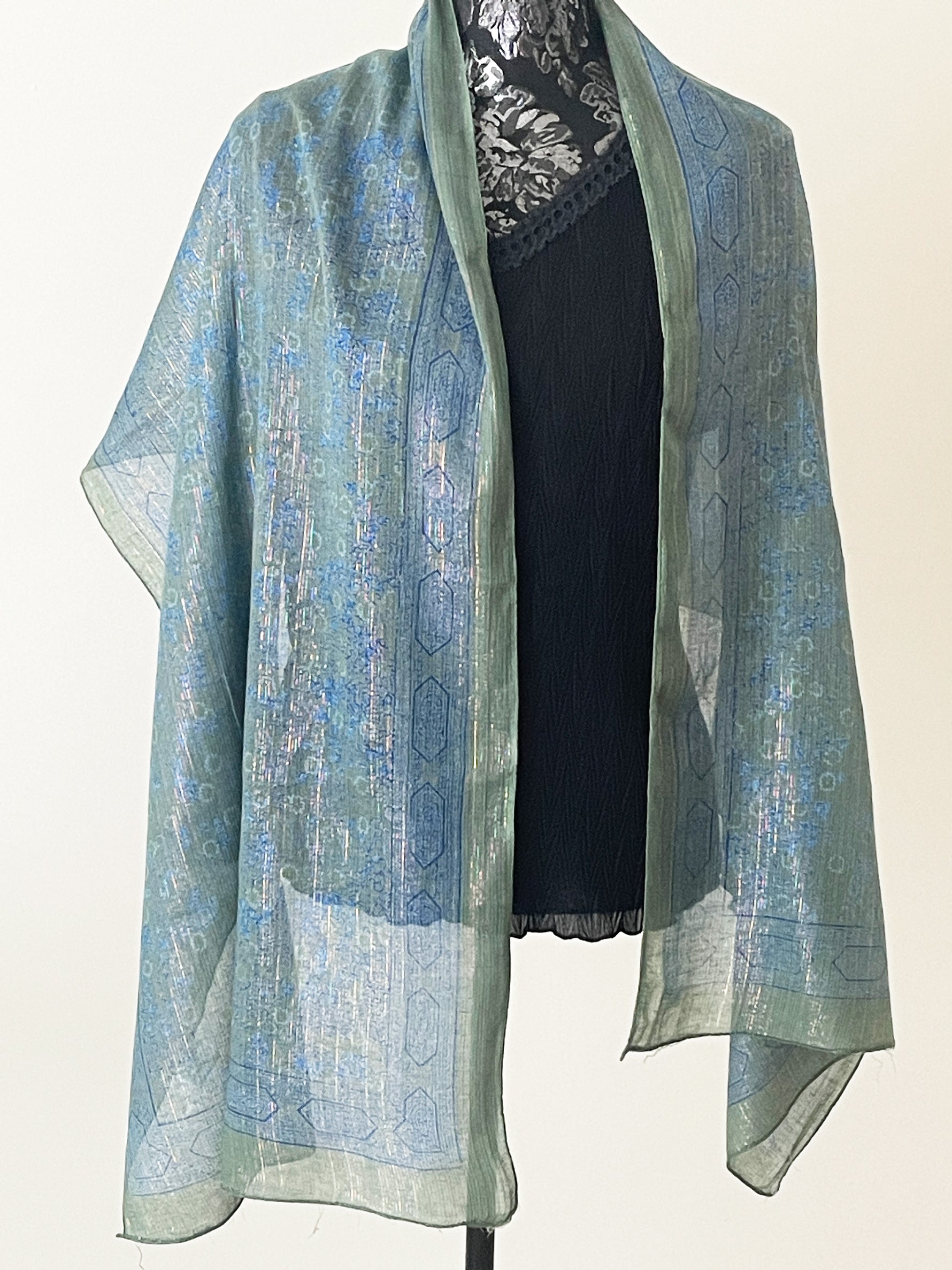 Teal coloured printed scarf woven with sparkly lurex threads draped over a black top.